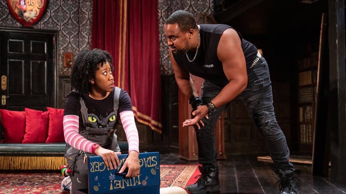 A person leaning down and talking to another person with red drapes and a couch in the background